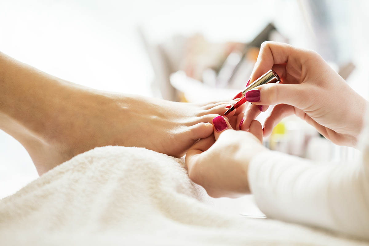 Une pédicure pose du vernis à ongles sur des orteils